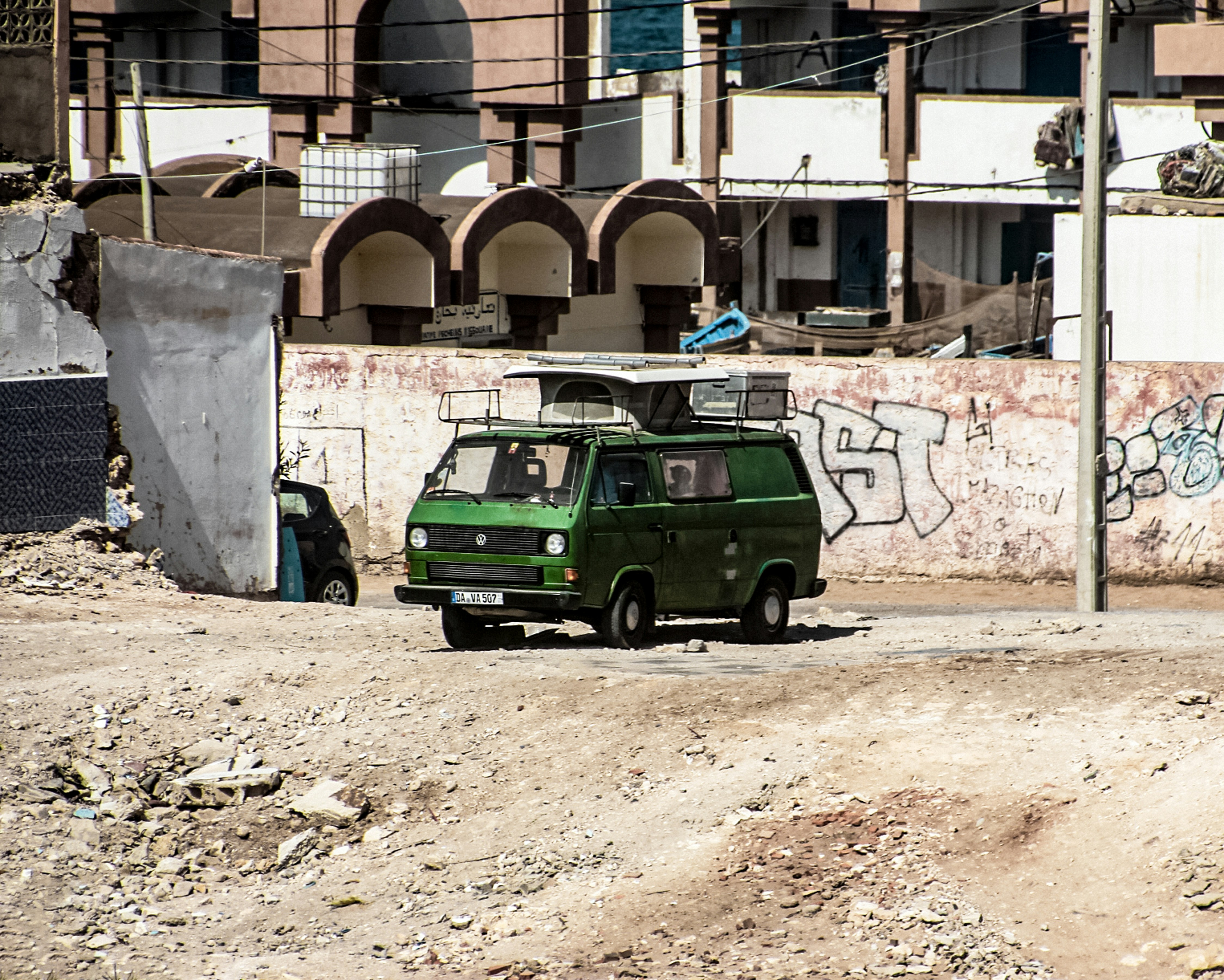 a green van parked in front of a building, Old green parked campervan in Imsouan. Imsouan, a small coastal town located 90 km north of Agadir, is also known as a charming fishing village. From my very first steps in this amazing village and my initial small talks with the locals, I felt the good vibes they shared with visitors. Imsouan is a famous tourist destination, beloved by surfers from around the world for its bay, its large waves, and its relaxing, calm atmosphere.