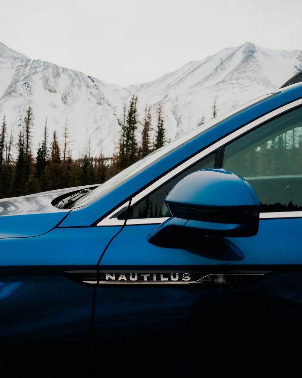 a blue car parked in front of a snow covered mountain