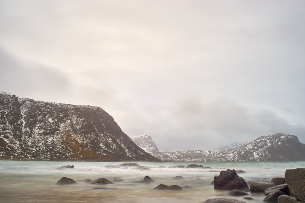 a rocky beach with snow covered mountains in the background