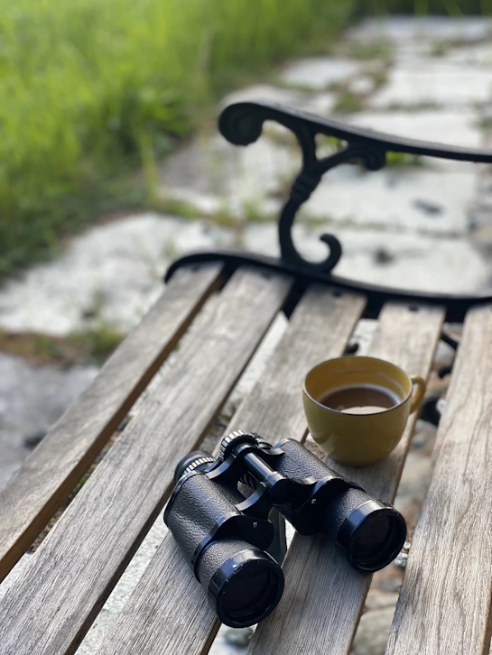 a cup of coffee and binoculars on a bench