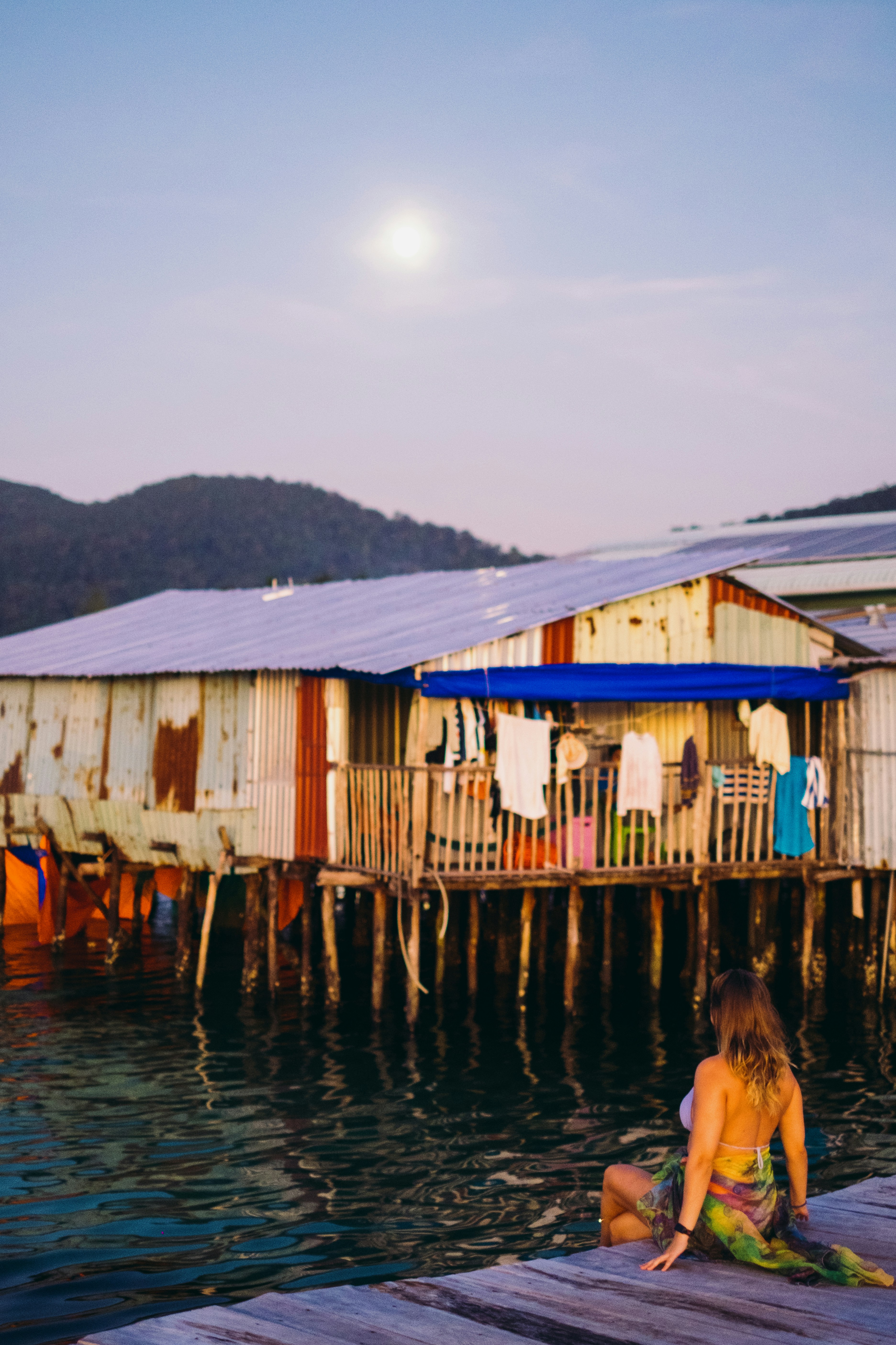 Una mujer sentada en un muelle frente a una choza