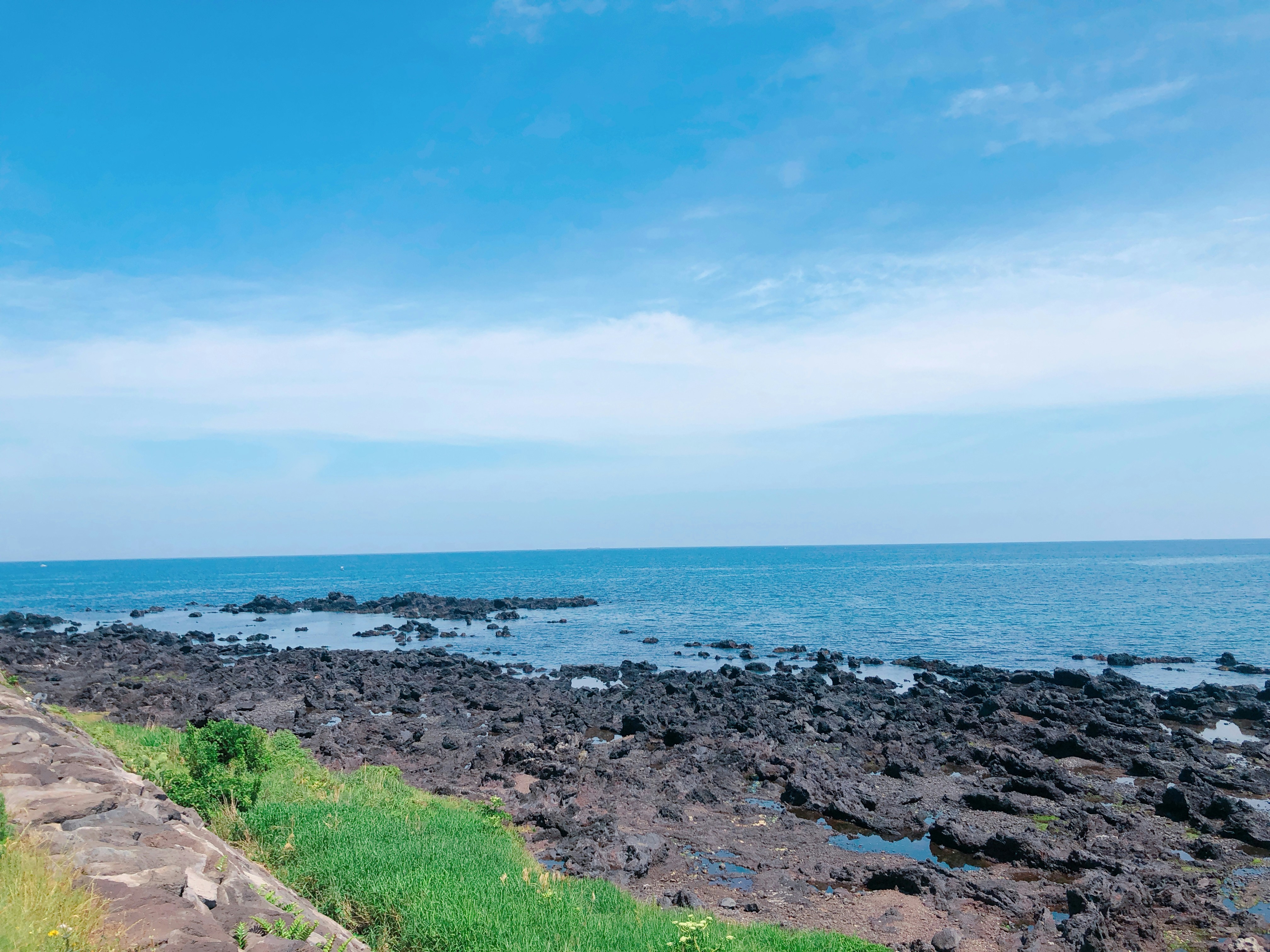 a man riding a bike down a rocky road next to the ocean, An image of a sea with shores of dark-clored rocks