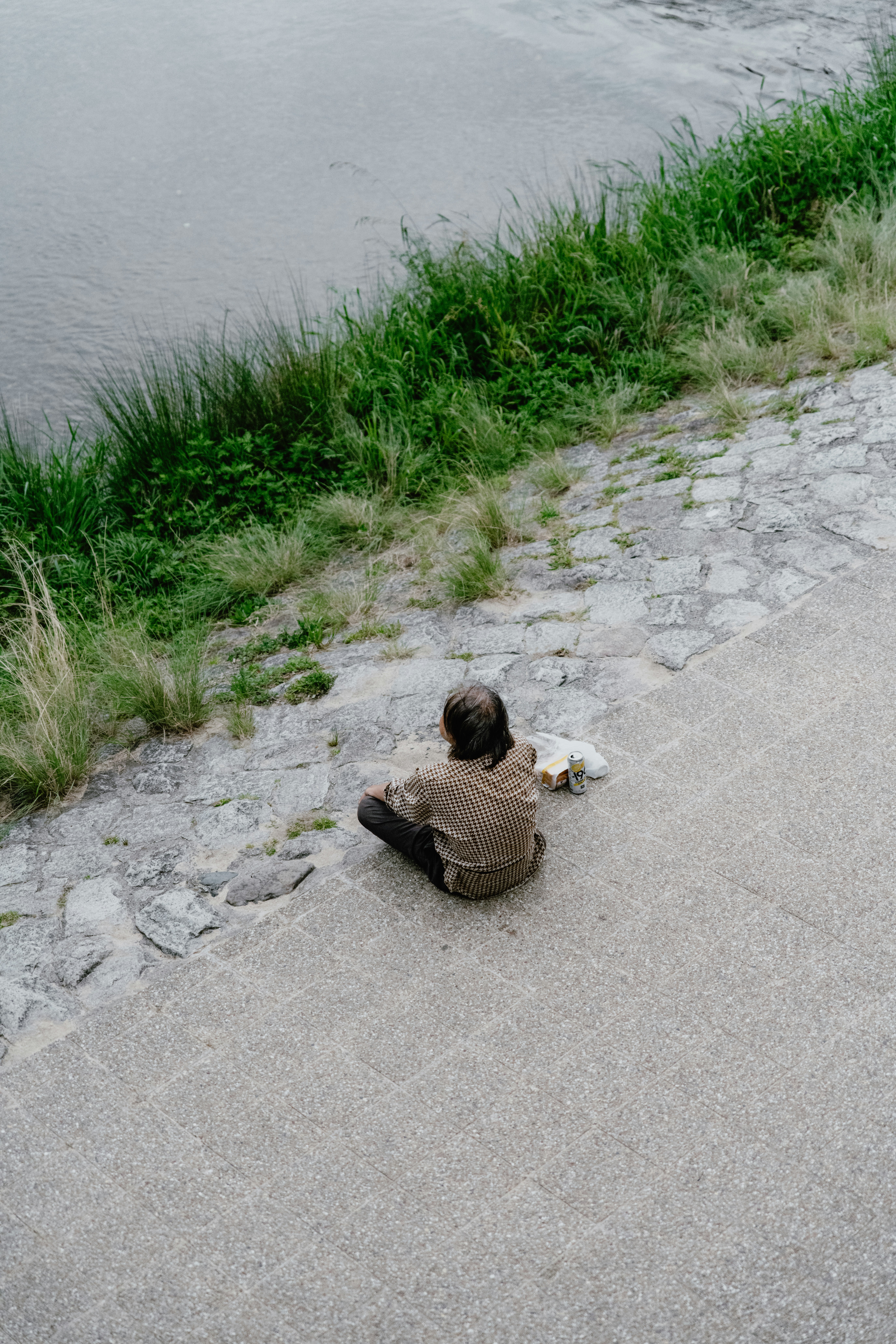 uma pessoa sentada no chão ao lado de um corpo de água