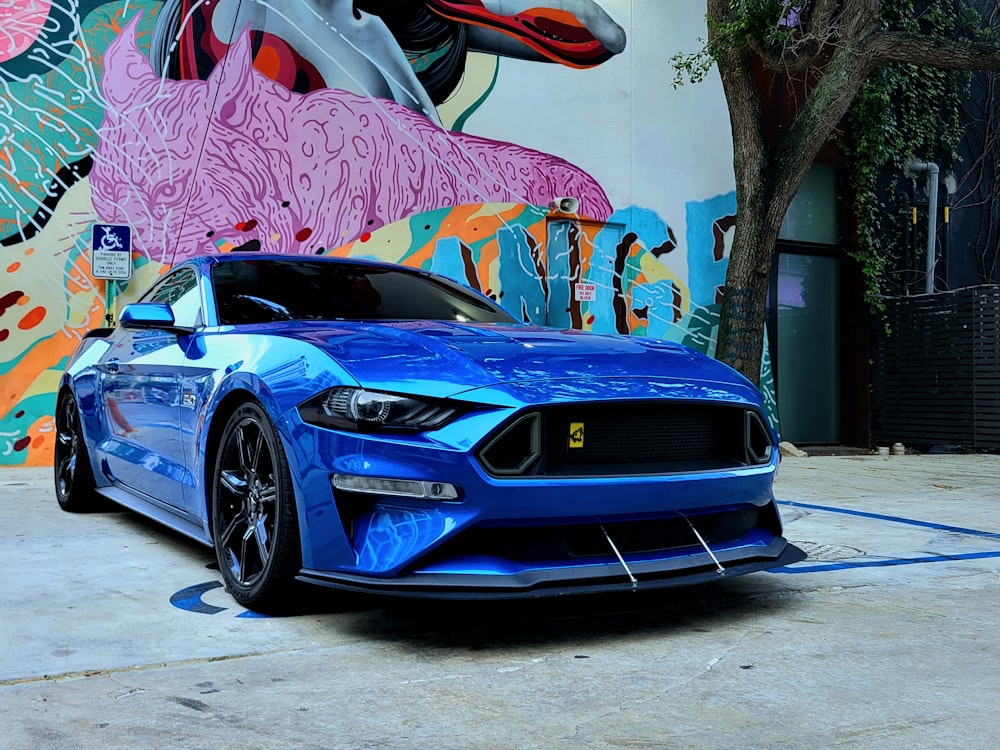 a blue mustang parked in front of a colorful wall