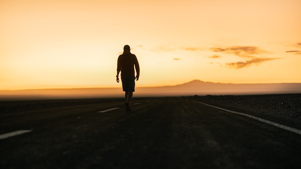 a man walking down a road at sunset