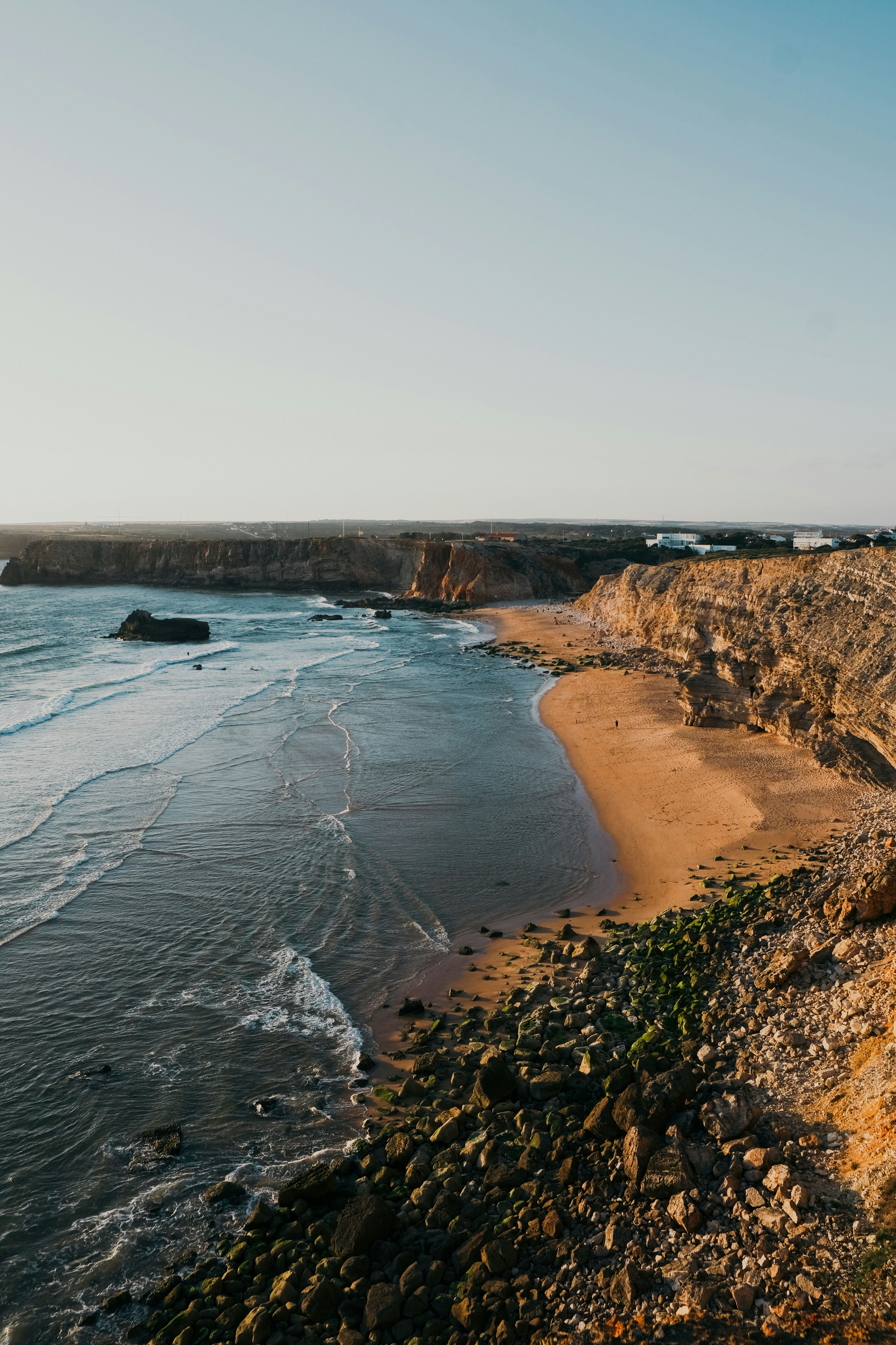 a sandy beach next to the ocean under a blue sky