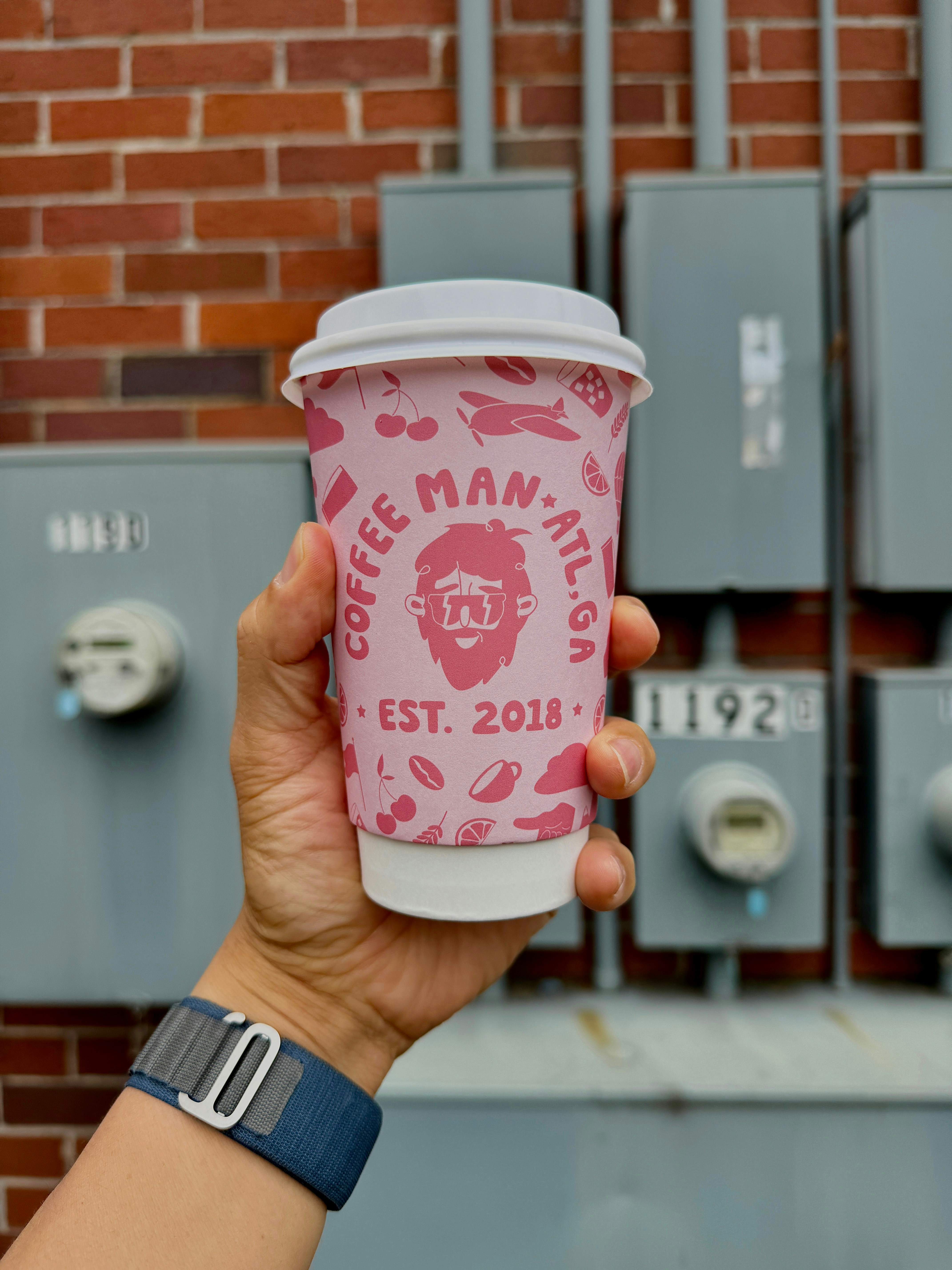 a person holding a cup of coffee in front of a brick wall