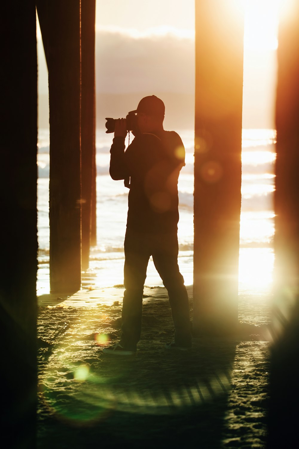 a man standing under a pier with a camera