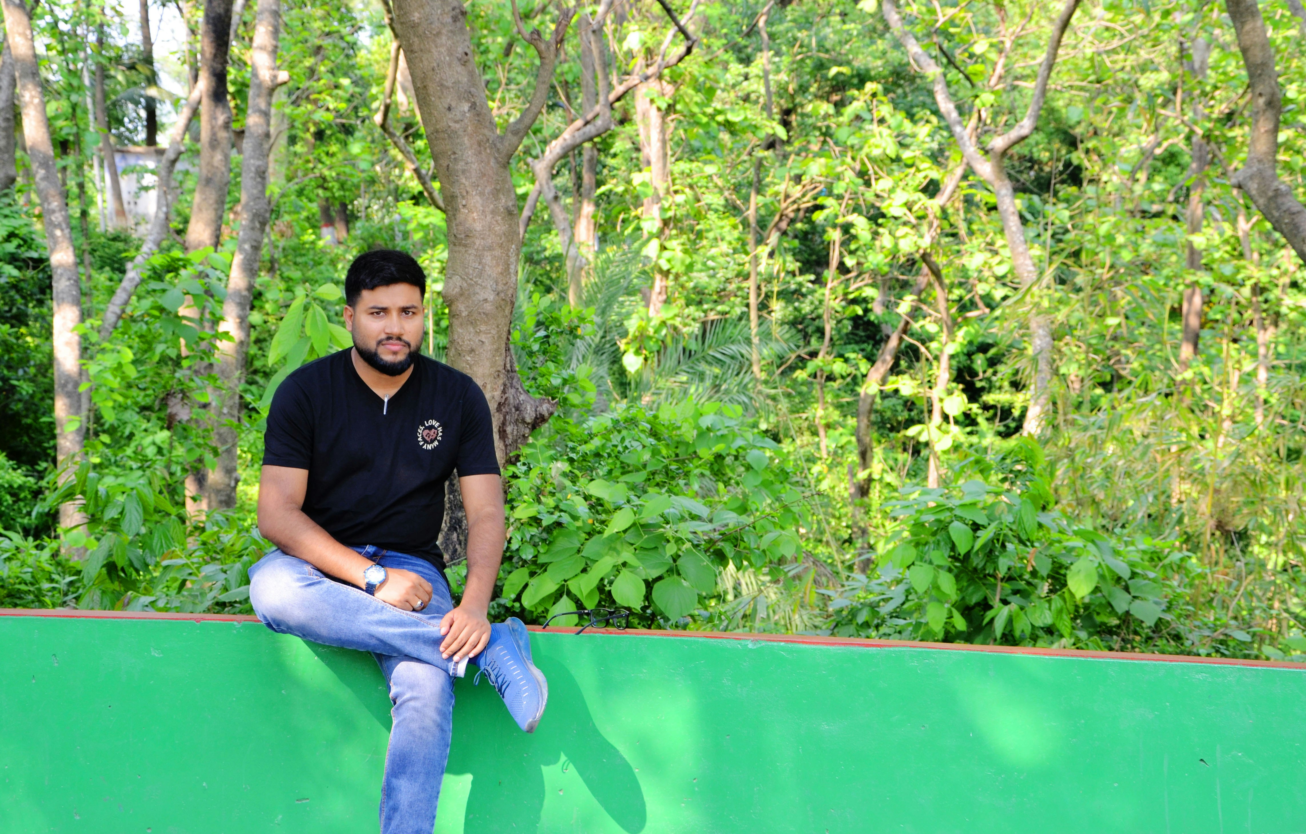 나무를 배경으로 녹색 벽에 앉아 있는 남자