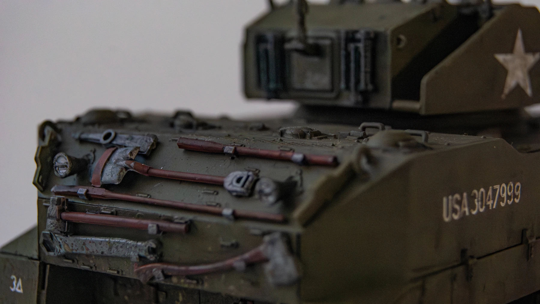 Close-up of an olive model tank's rear hull, with pioneer tools, a white star and a painted serial number