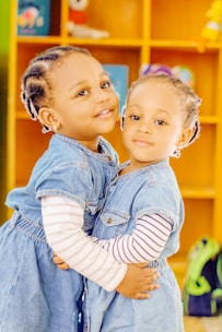 two young girls hugging each other in front of a bookshelf