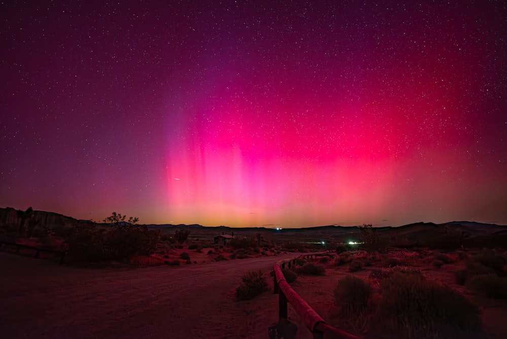 a bright pink and purple aurora over a dirt road