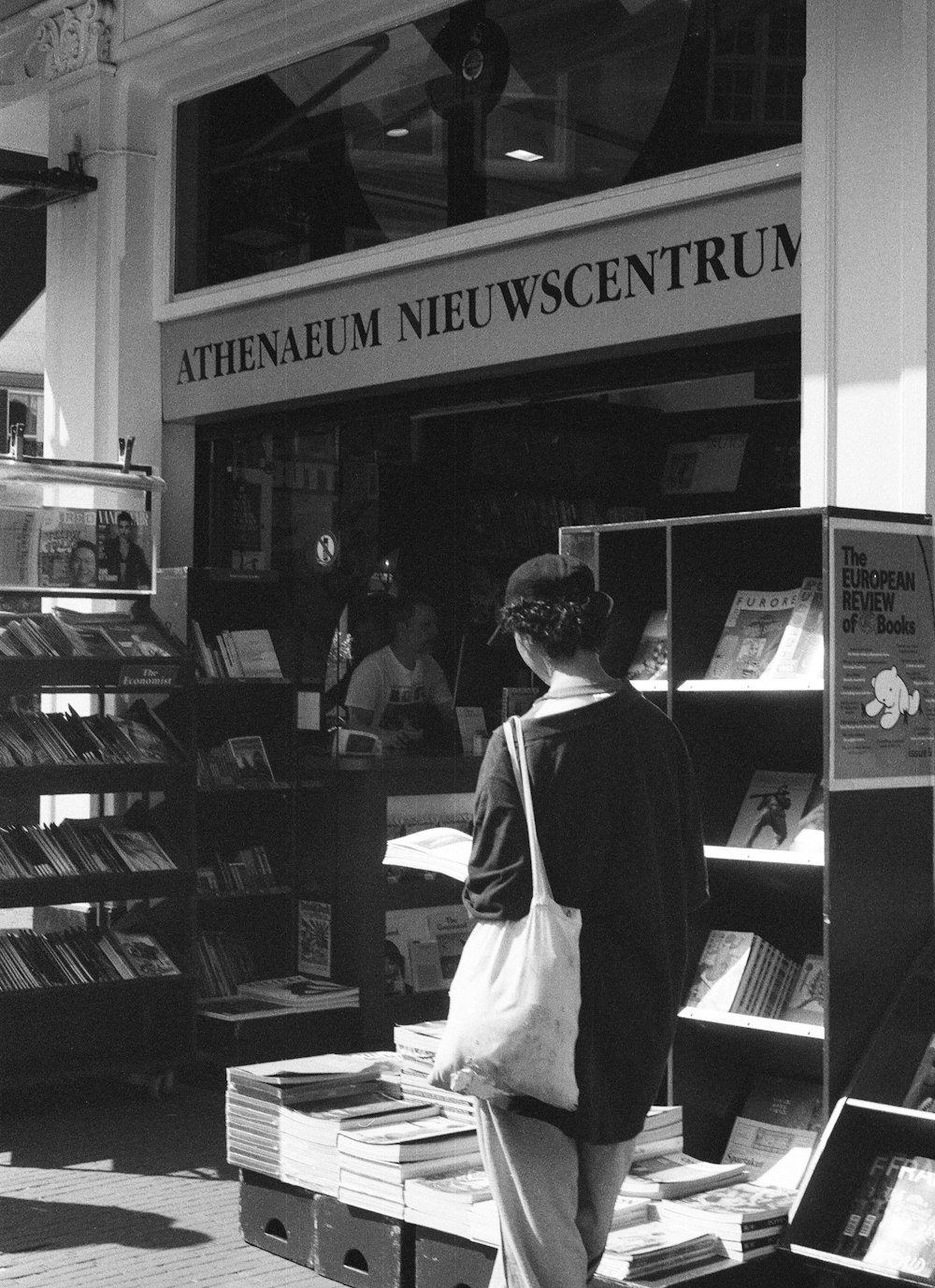 a black and white photo of a woman standing in front of a book store