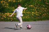 a young boy kicking a soccer ball on a road