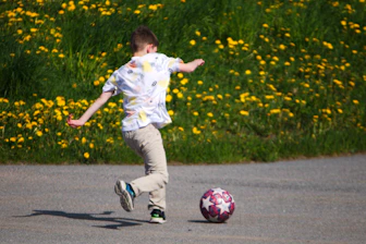a young boy kicking a soccer ball on a road