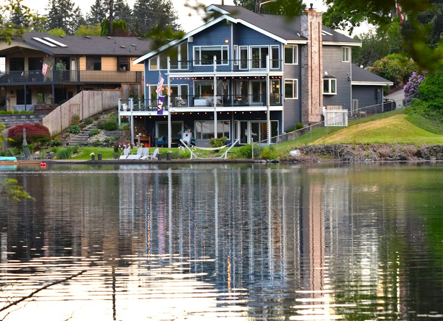 Blue-grey three-storey home with stacked decks, reflected in still water on a calm evening