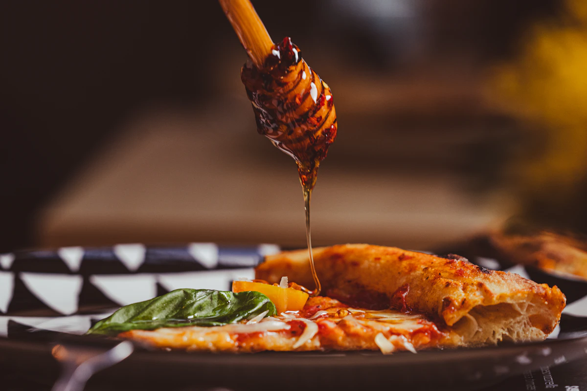 Honey being drizzled from a dipper over a hot pepperoni pizza