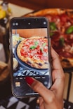 a woman taking a picture of a pizza on her phone
