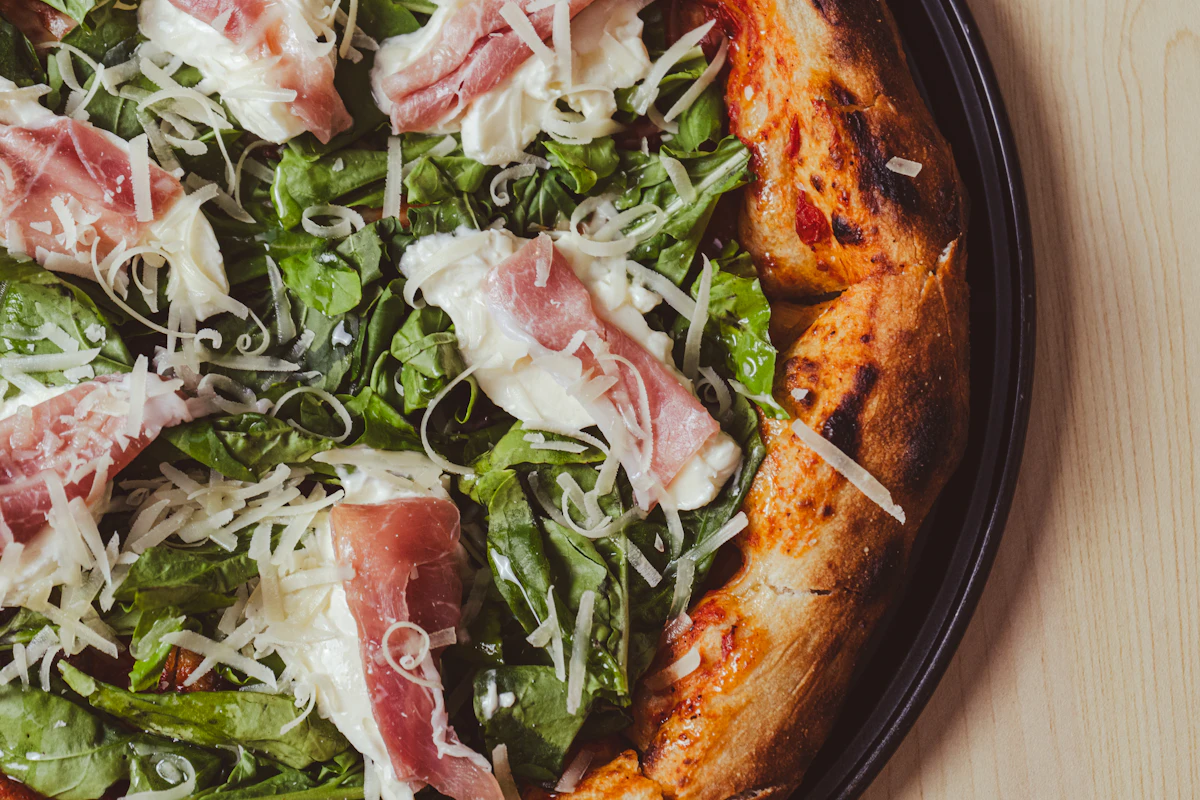 Pizza topped with draped prosciutto and a pile of dressed arugula