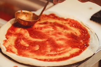 a person making a pizza with sauce on it