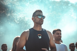 a man in a tank top and sunglasses standing in front of a group of people