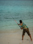 a young boy holding a fishing rod on the beach