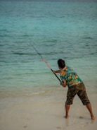 a young boy holding a fishing rod on the beach