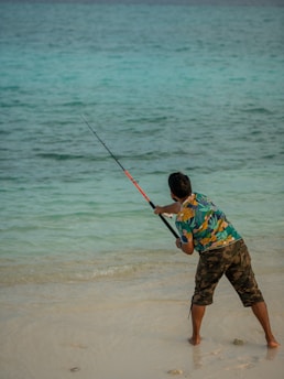 a young boy holding a fishing rod on the beach