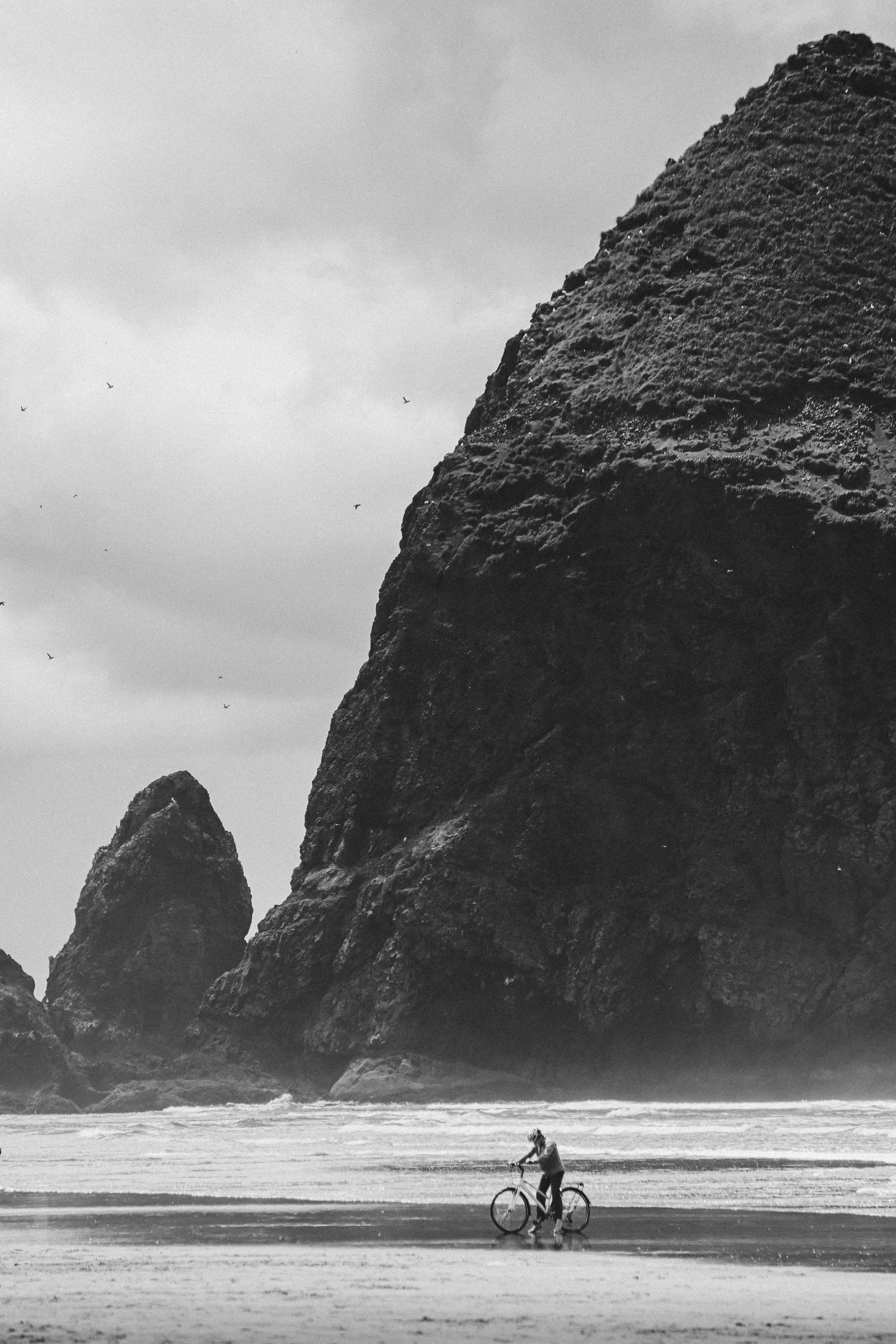a black and white photo of a person riding a bike on the beach