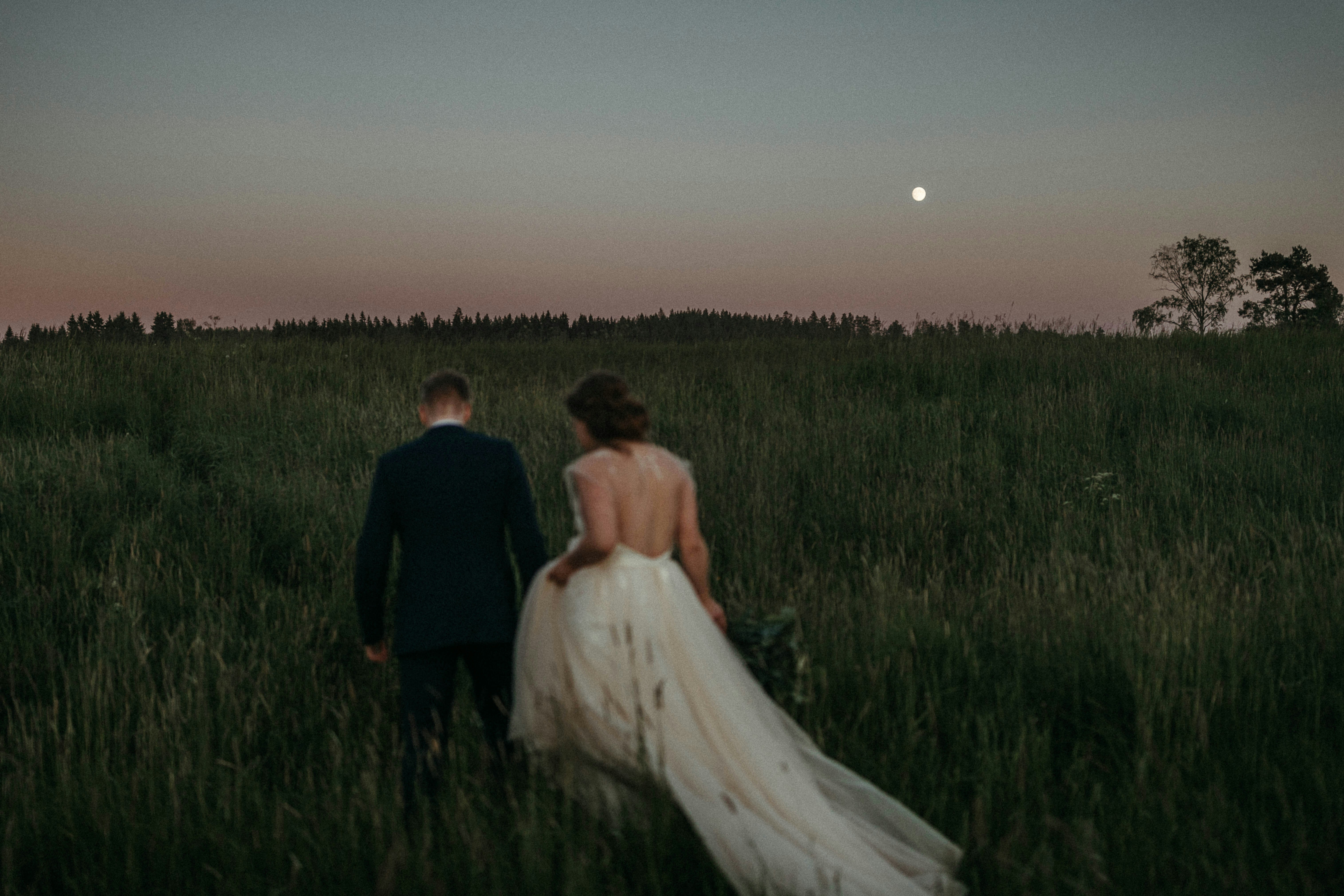 a bride and groom walking through a field at sunset