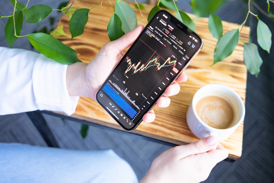 a person holding a cell phone in their hand, Crypto trader investor analyst businessman using mobile phone app analytics for cryptocurrency financial market analysis, chart graph index on smartphone. Hands holding phone and cup of coffee.