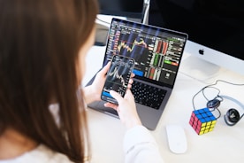 Uma mulher sentada com seu laptop e um celular na mão acompanhando o mercado financeiro.