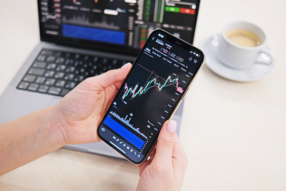 Persona analizando datos financieros en teléfono con gráficas de mercado frente a una computadora — así se ve invertir en ETFs desde México con apps como GBM+