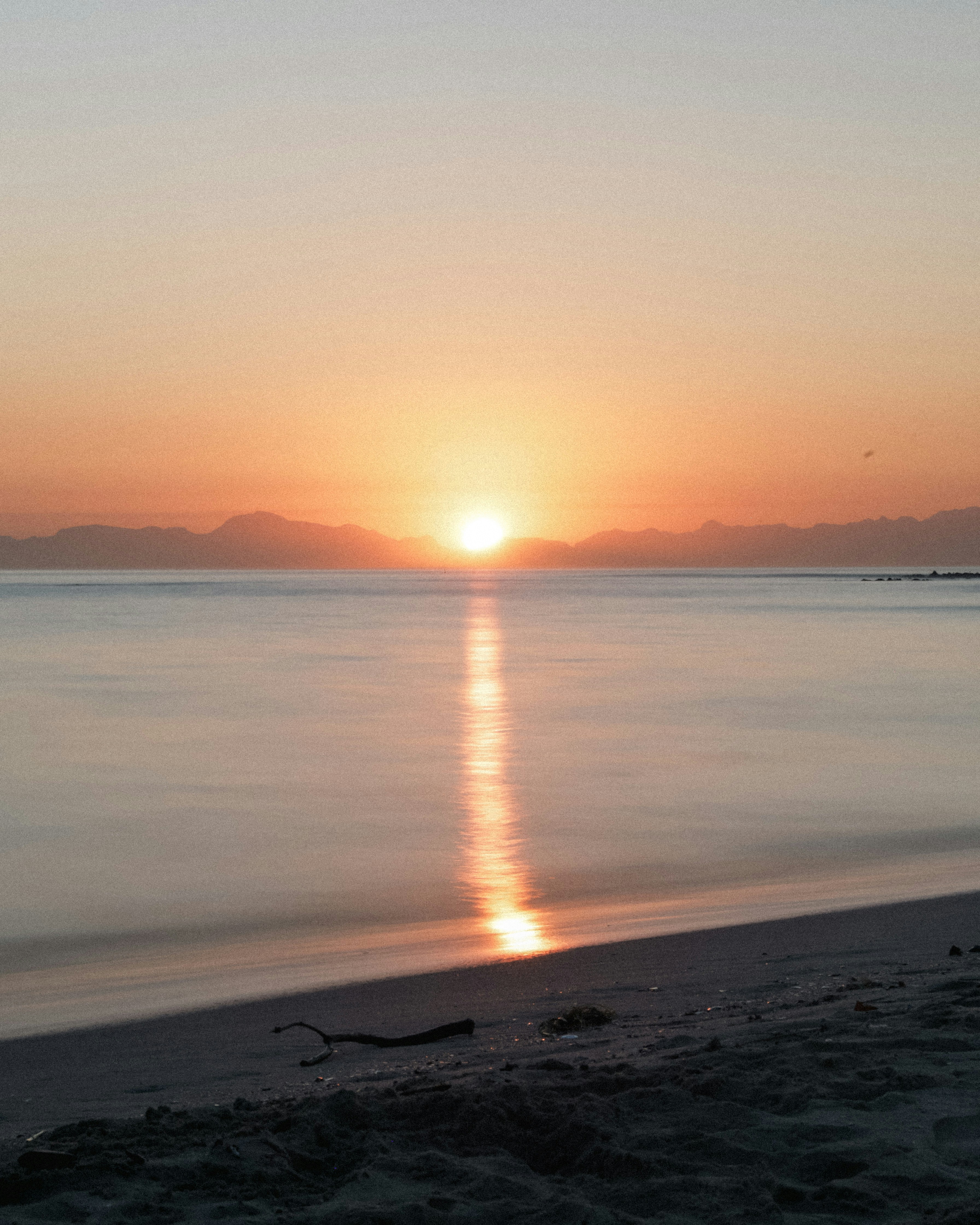 the sun is setting over the water on the beach
