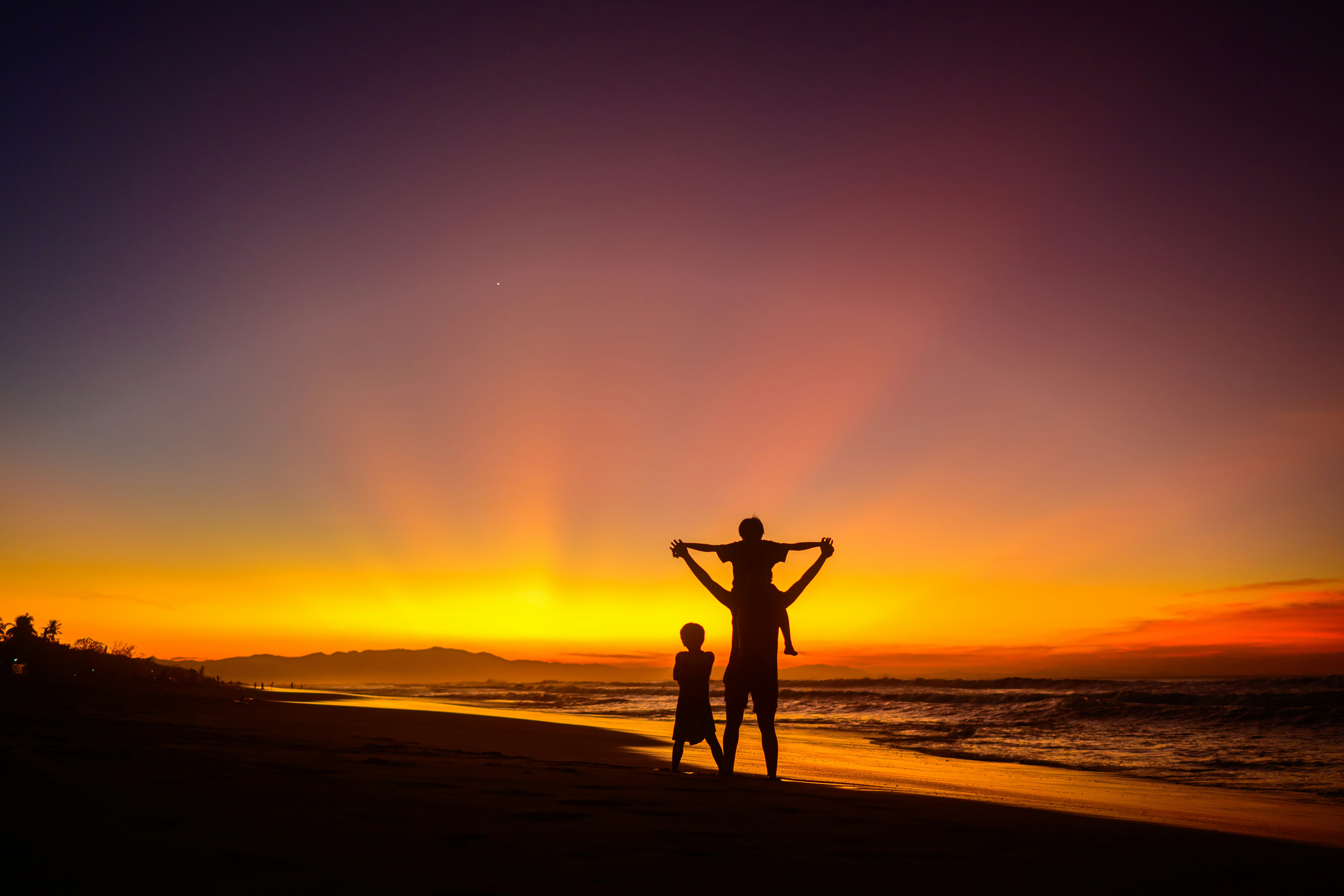 Family silhouettes on tropical beach at sunset, dark warm horizon, deep orange glow, atmospheric tropical dusk with long shadows
