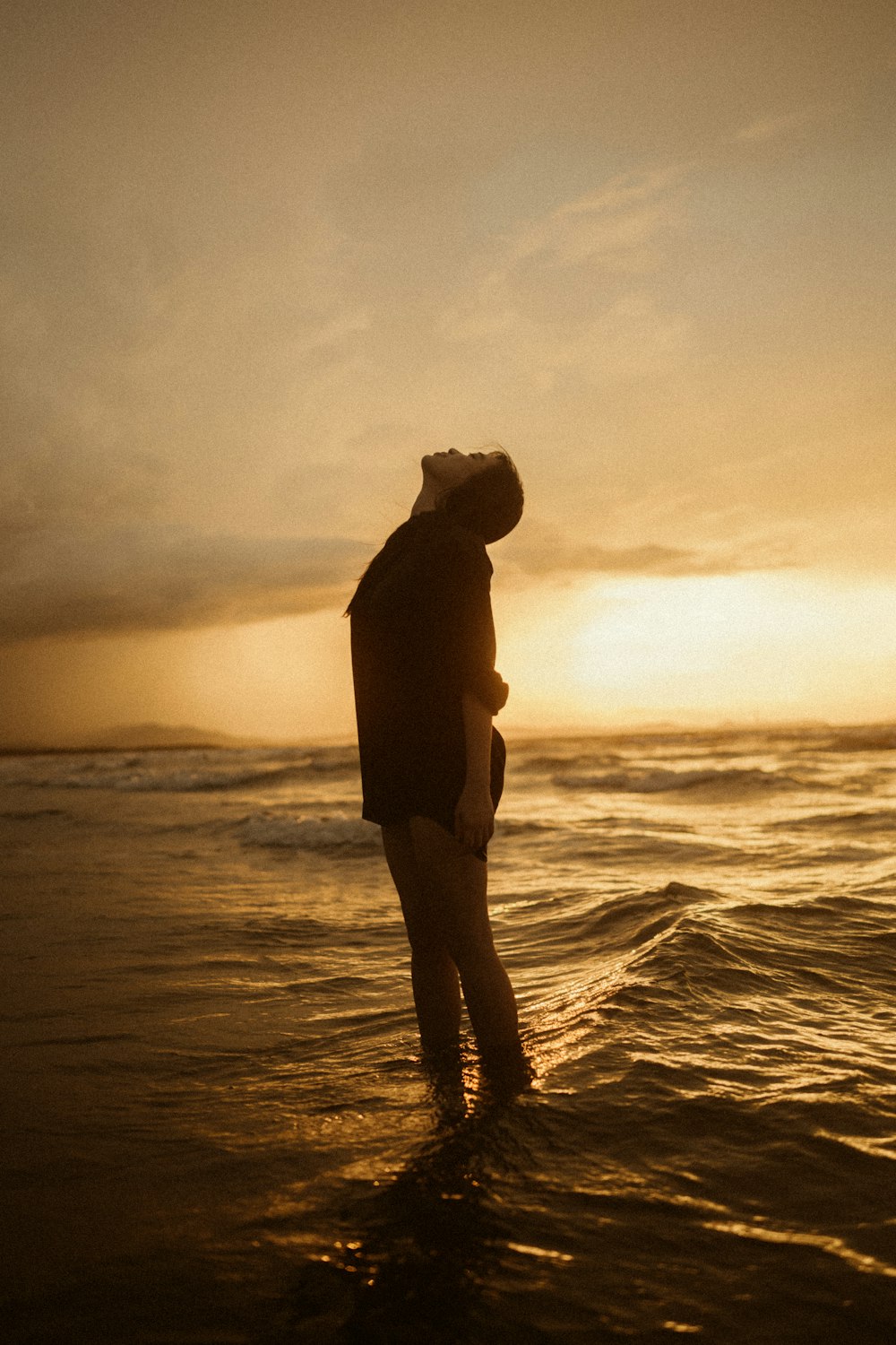 a man standing in the ocean at sunset