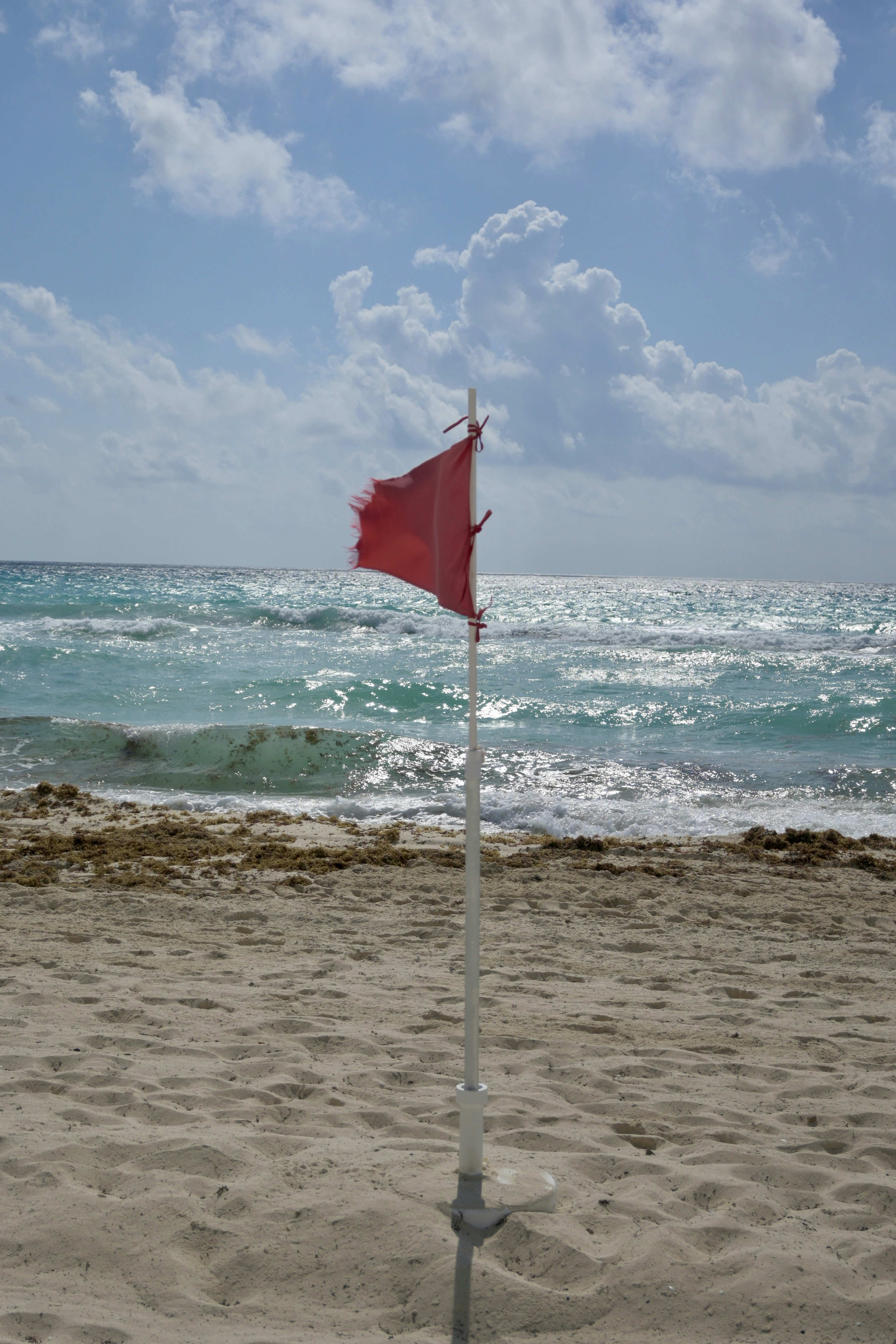 a red and white flag on a beach next to the ocean