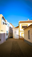 a cobblestone street lined with white and yellow buildings
