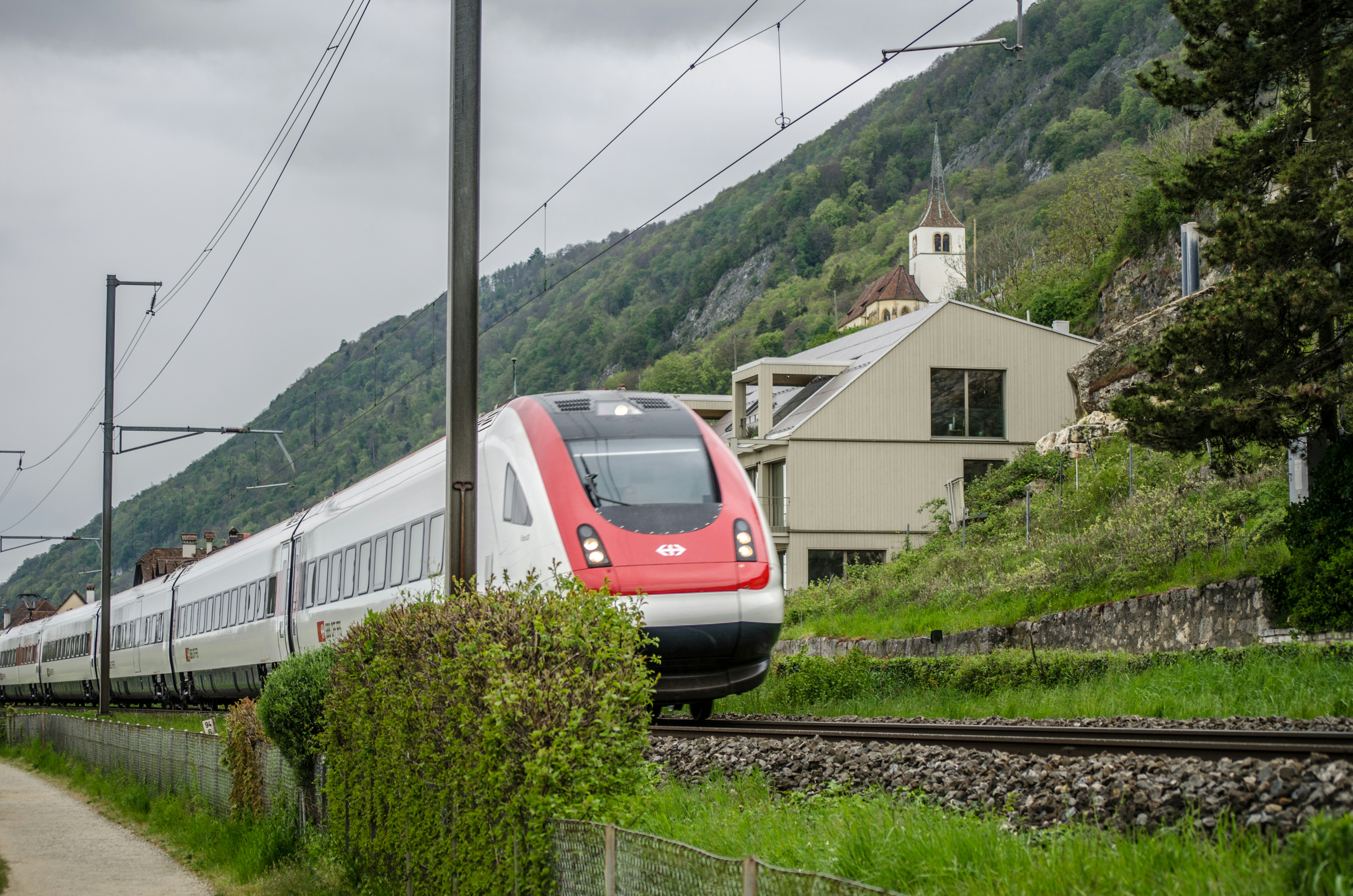 A red and white train traveling past a lush green hillside photo – Free ...