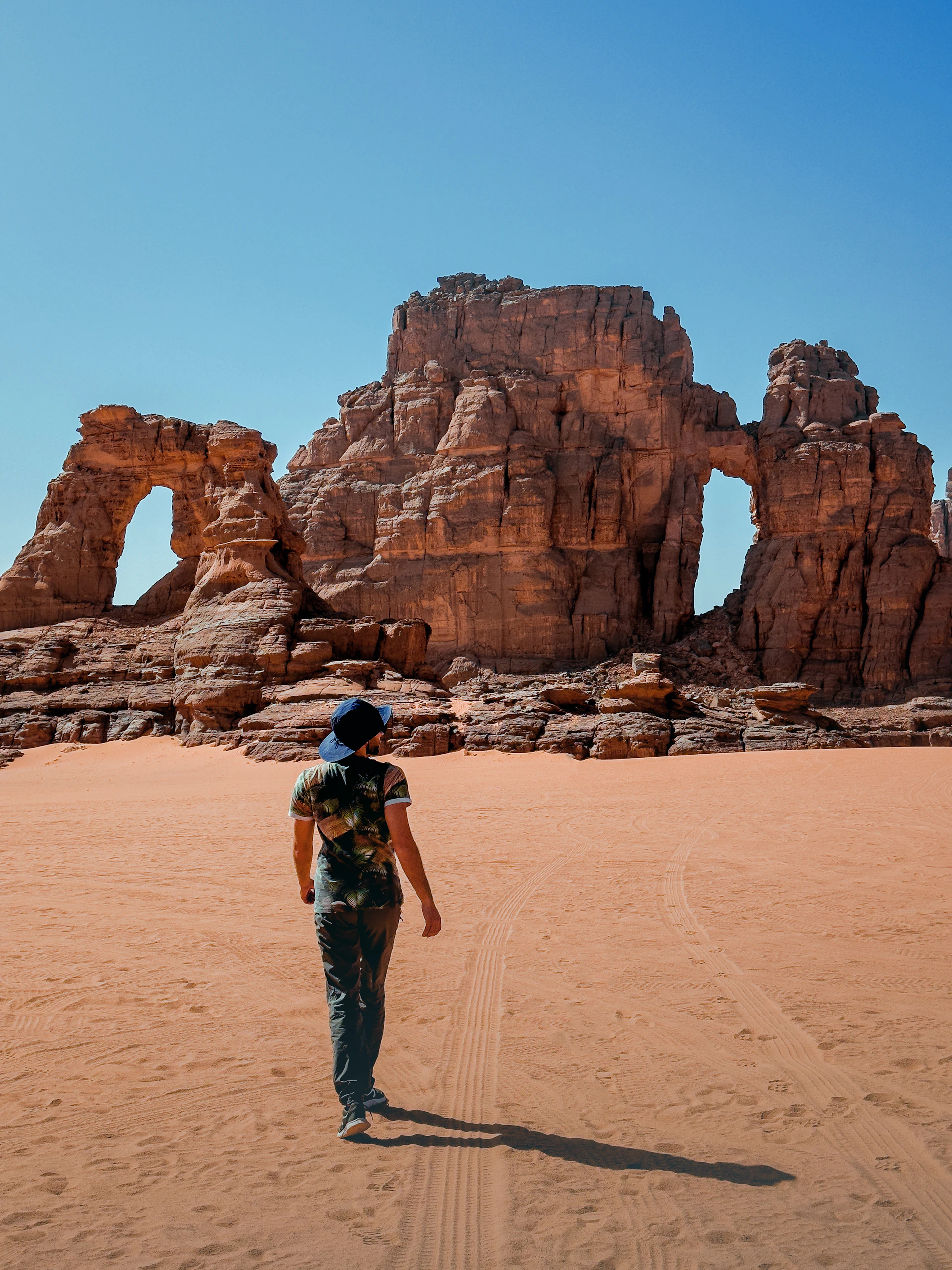 a man walking across a sandy field next to a rock formation