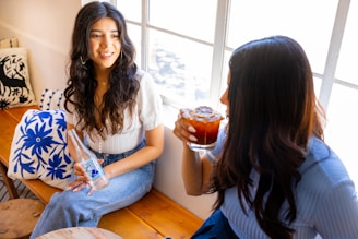 two women sitting on a window sill drinking beverages
