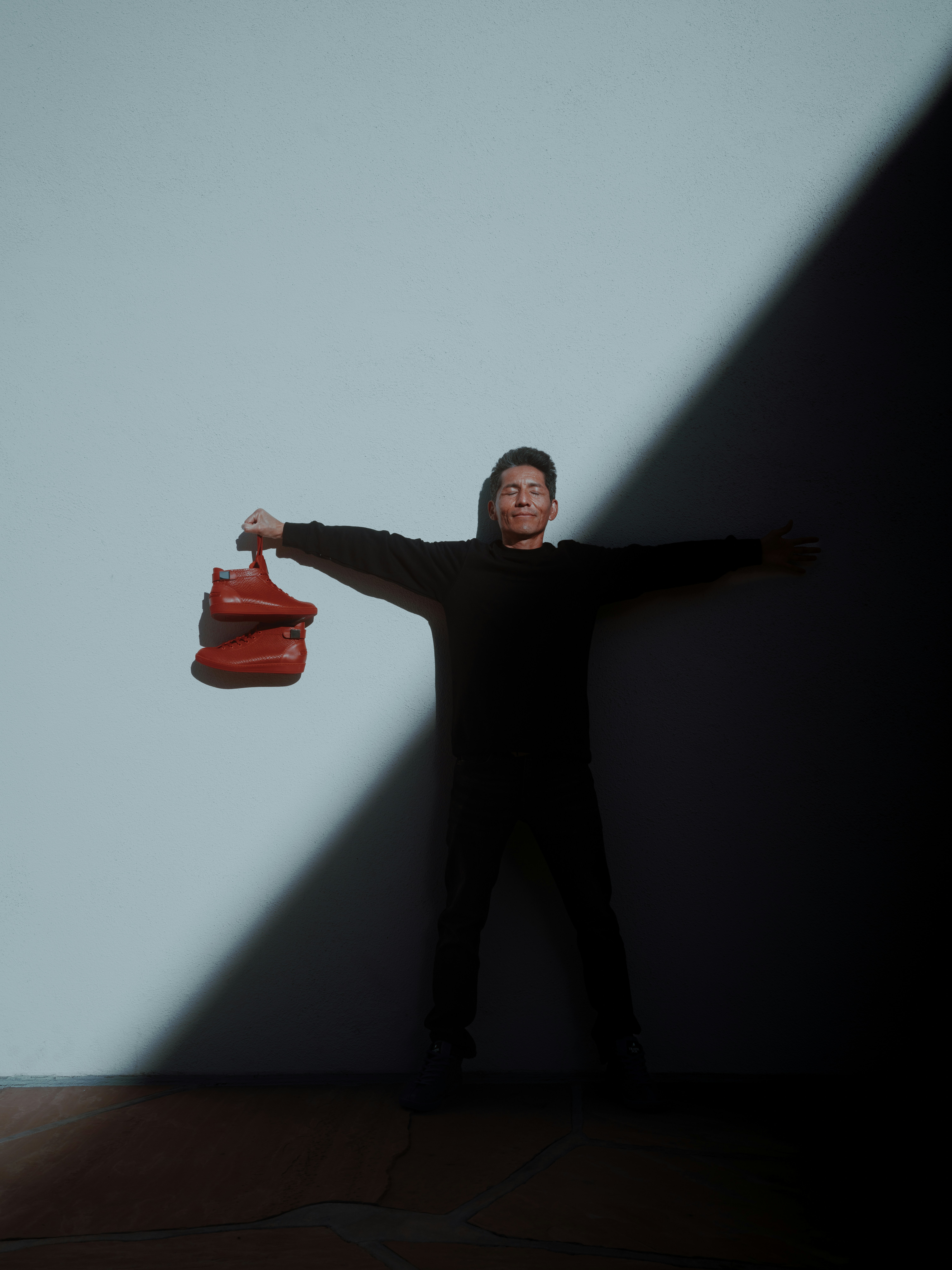 un uomo in piedi di fronte a un muro bianco con in mano una borsa rossa