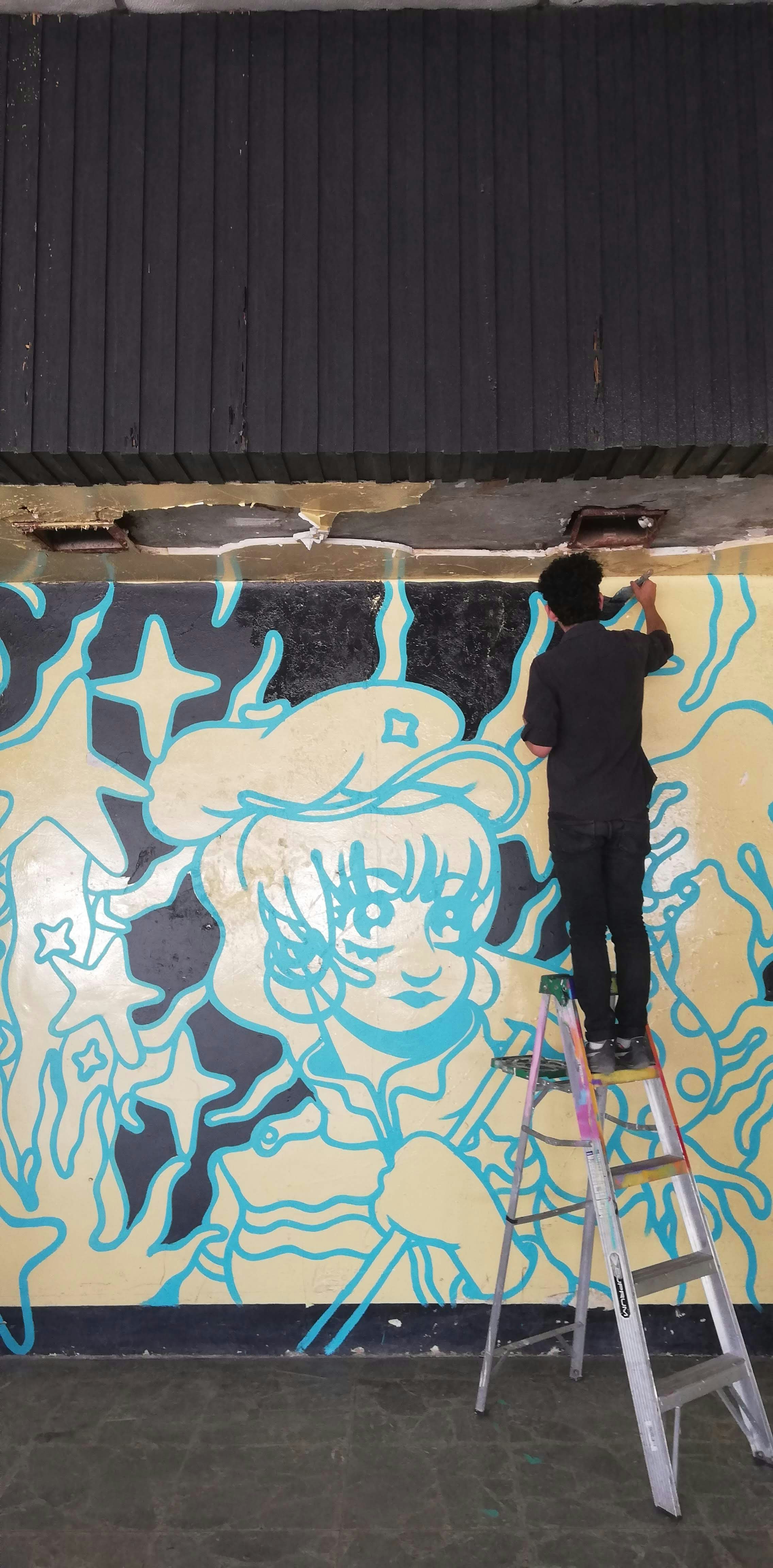 a man on a ladder painting a mural on a wall