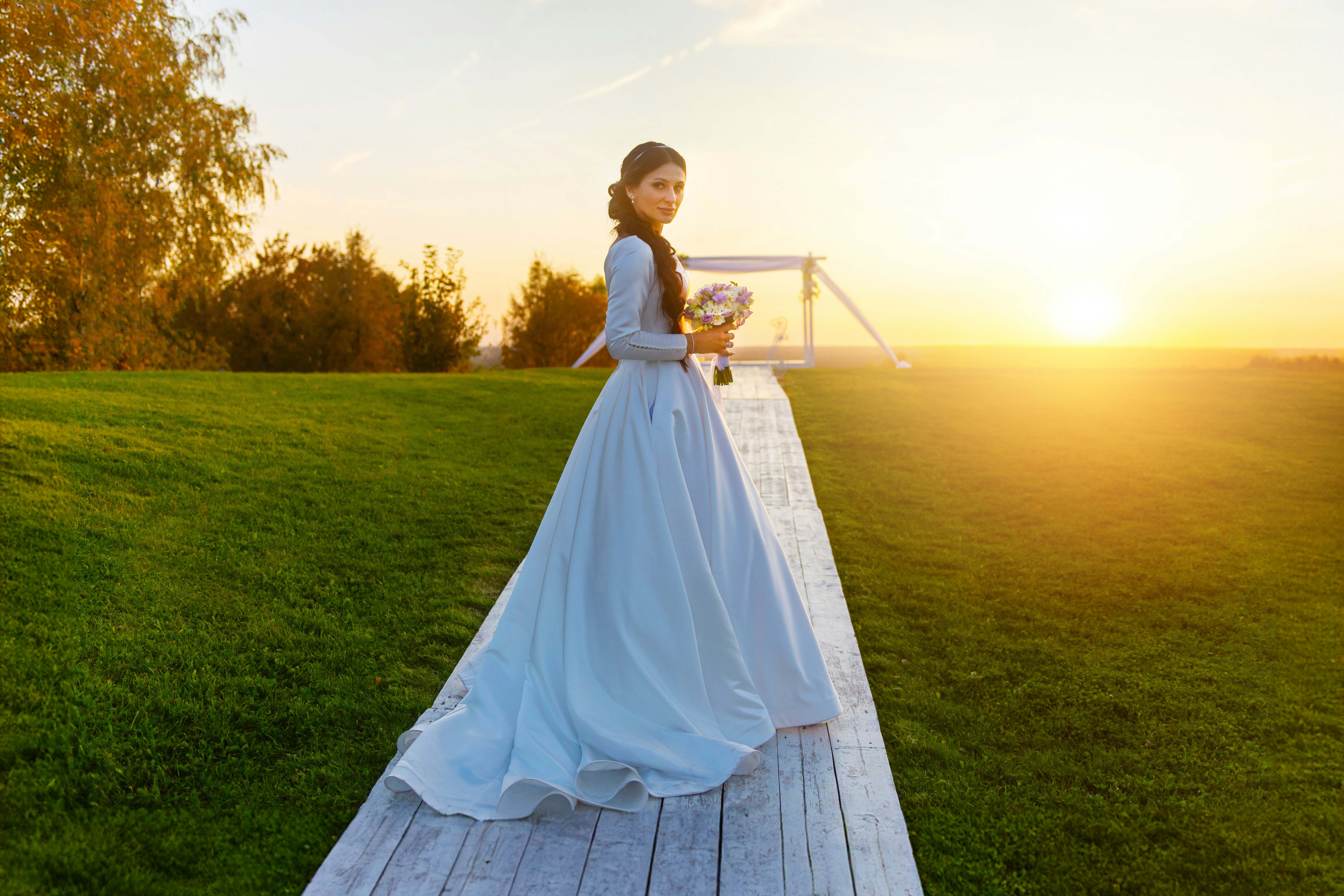 a woman in a wedding dress standing on a wooden walkway