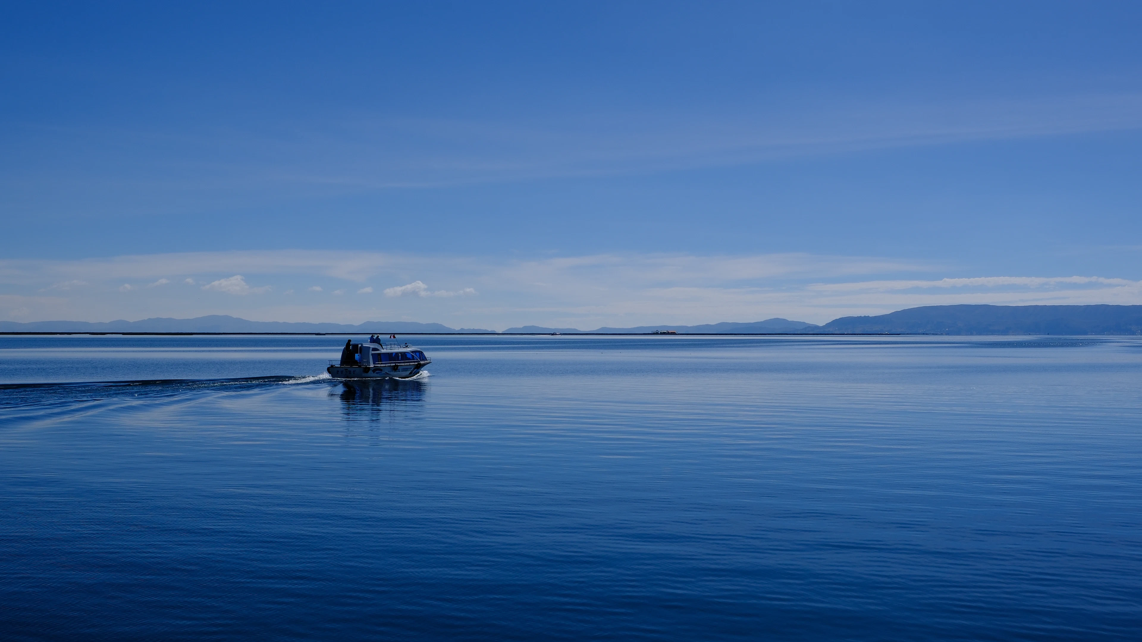 A small boat crossing the calm, deep-blue waters of Lake Titicaca in Peru