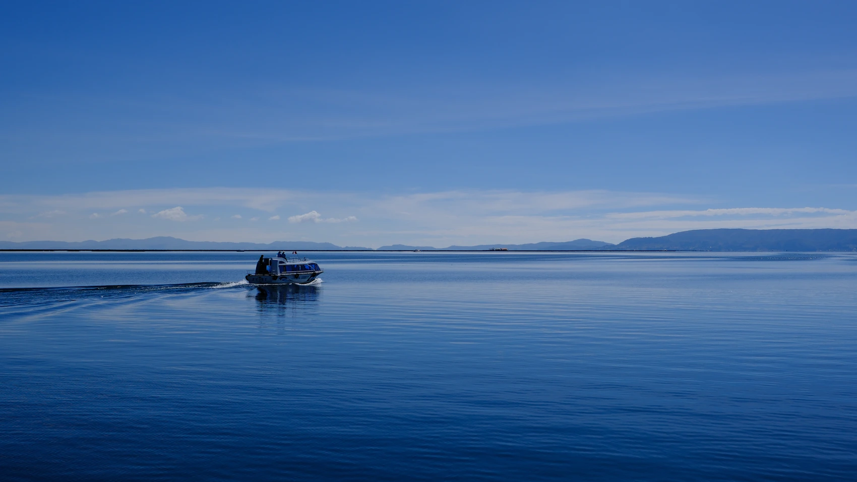 A small boat crossing the deep blue water of Lake Titicaca in Peru
