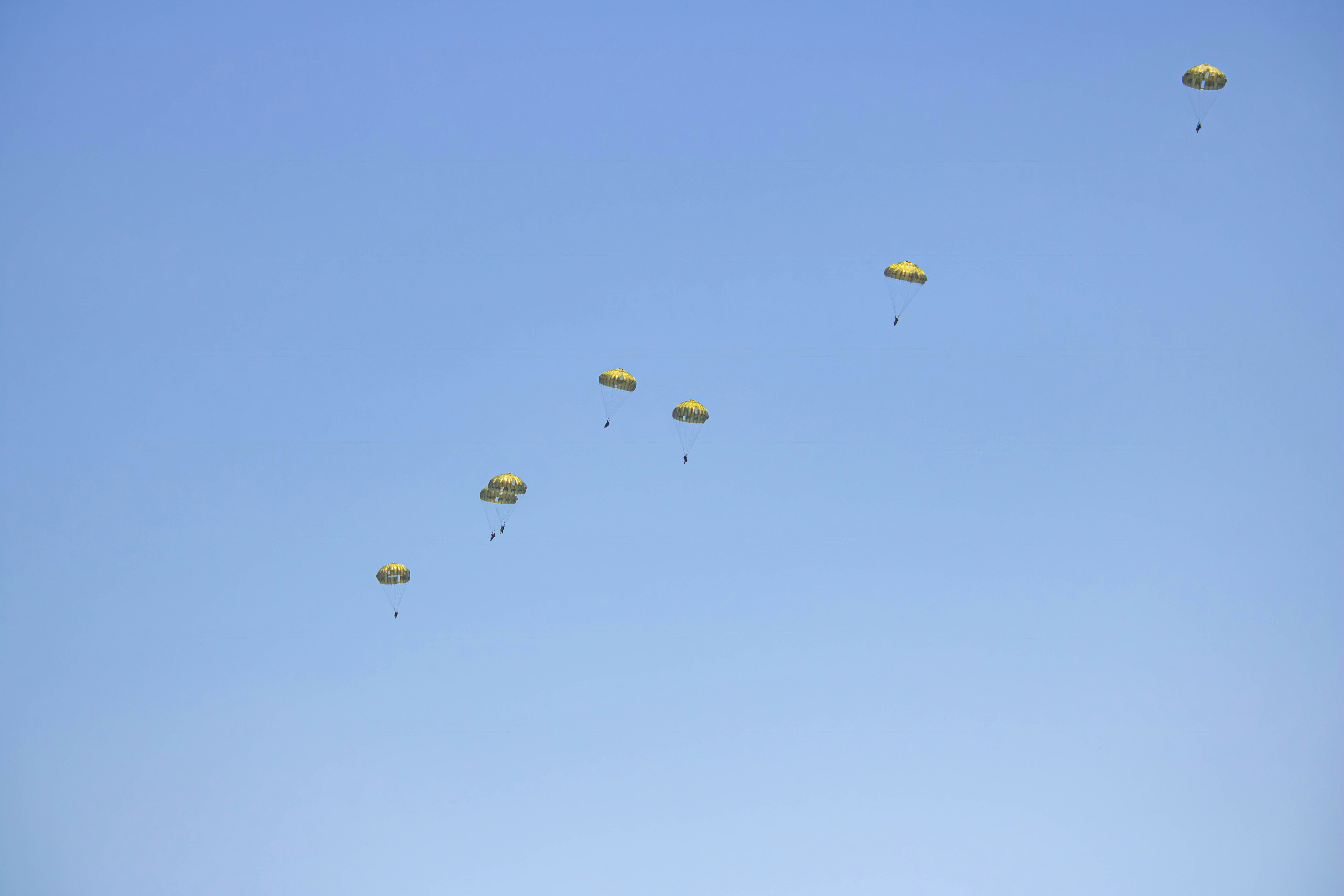 a group of yellow parachutes flying through a blue sky