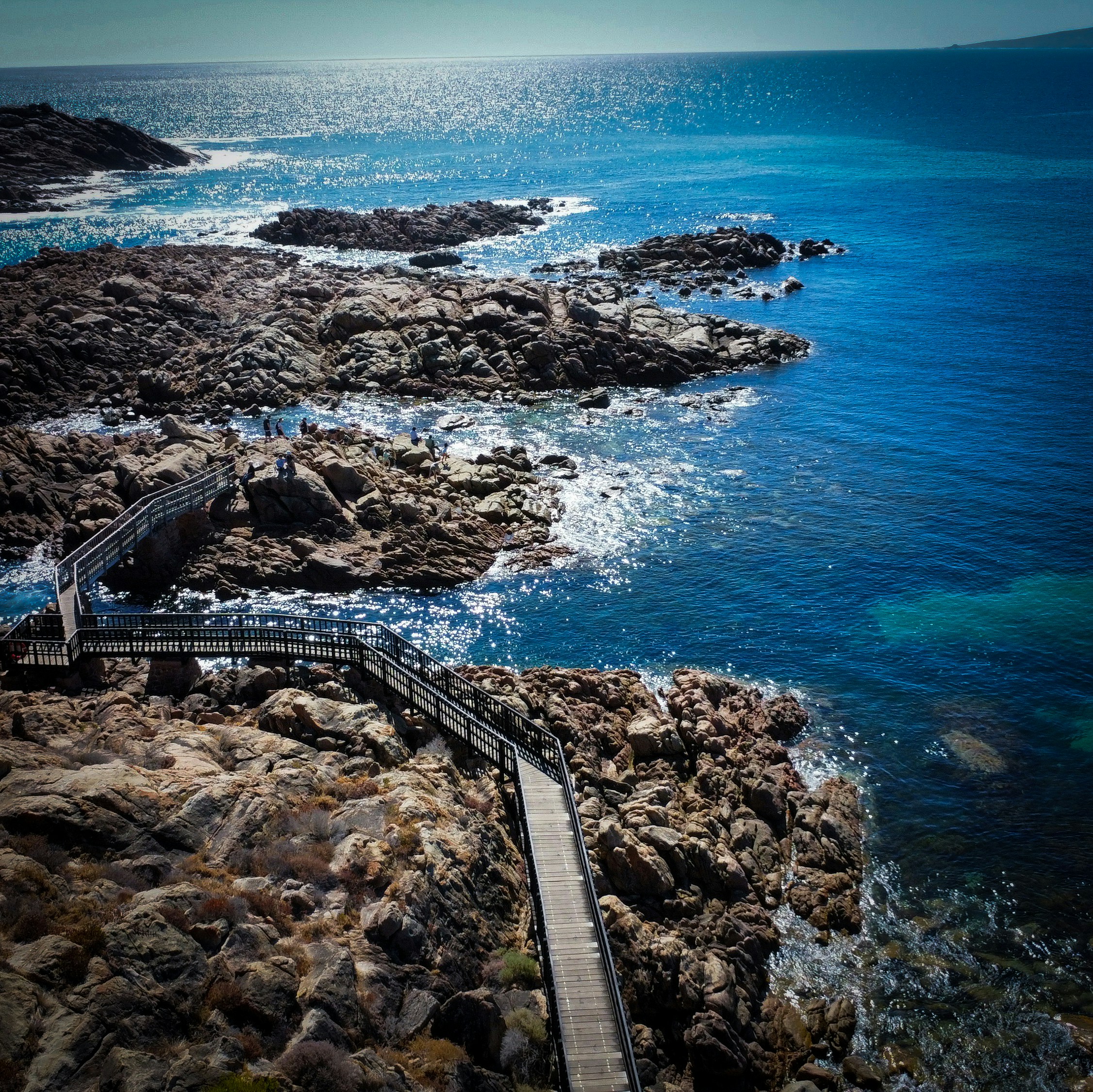 uma passarela de madeira que leva ao oceano ao lado de uma costa rochosa