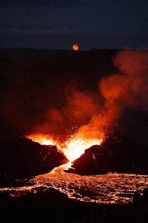 a lava flow at night with a full moon in the distance