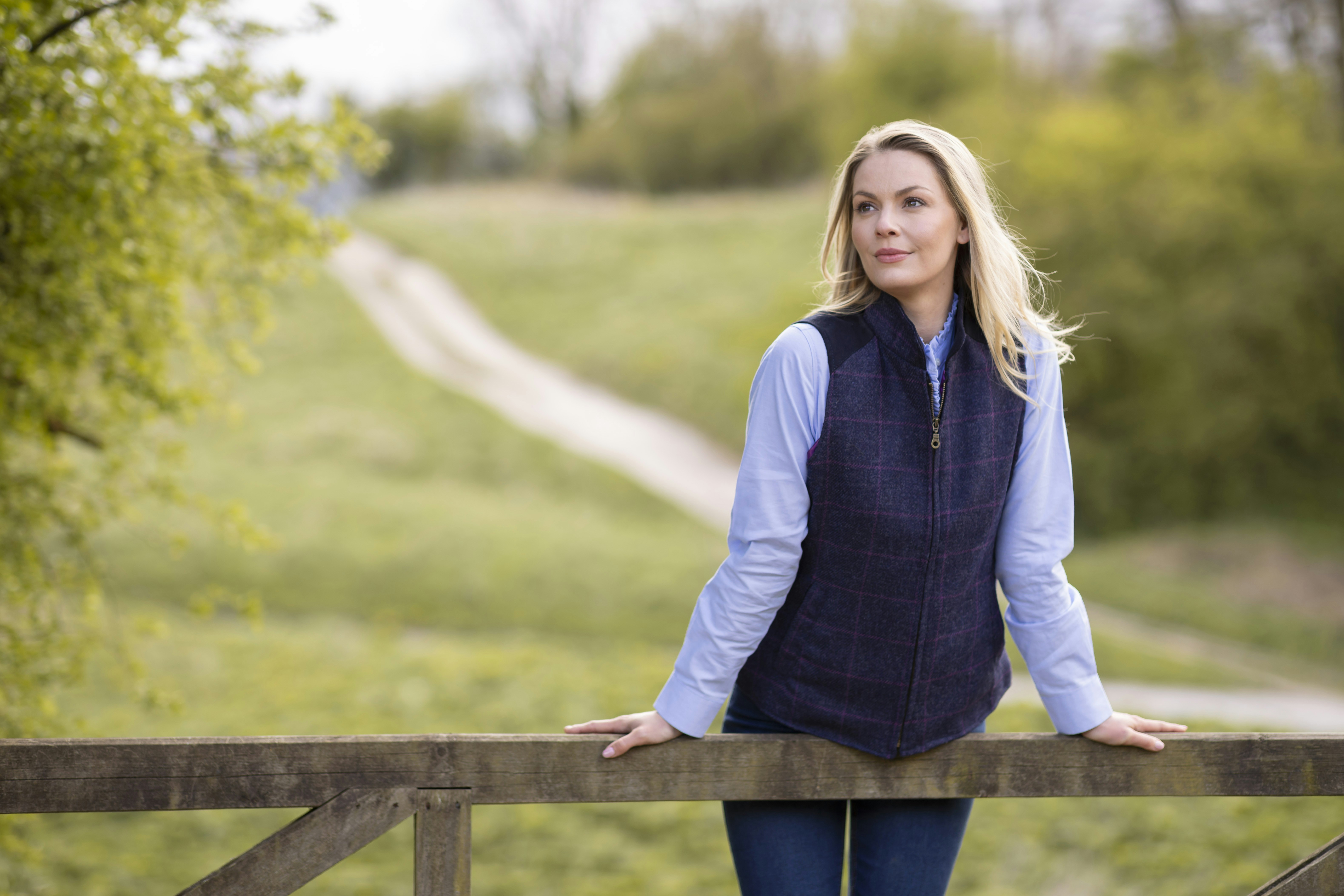 une femme appuyée sur une clôture en bois, les mains sur les hanches